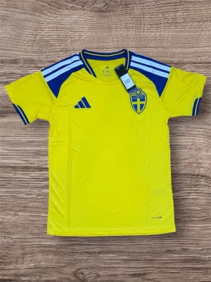 Svensk landslagströja Adidas gul/blå - Gul kortärmad landslagströja från Adidas med blå detaljer och Sveriges landslagsemblem på bröstet. Tröjan har rund hals, blå ränder på axlarna och blå muddar vid ärmsluten. Tillverkad i lätt och ventilerande funktionsmaterial.