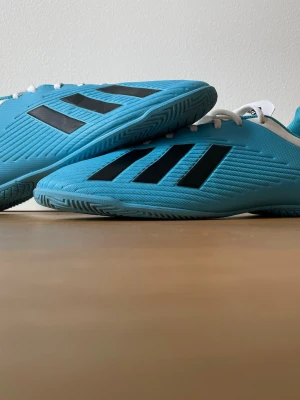 Blå Adidas fotbollsskor inomhus - Snygga blå fotbollsskor från Adidas med klassiska svarta ränder på sidan och vit häl. Skorna har låg profil, vita snören och är designade för inomhusspel. Tillverkade i syntetmaterial för bra grepp och komfort på planen. Andvända 2 gånger. Pris kan diskuteras.