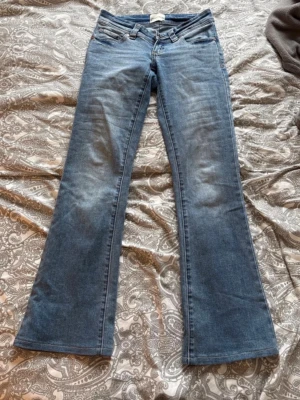 Blå bootcut jeans med låg midja - Säljer ett par klassiska blå bootcut jeans med låg midja och fem fickor. Jeansen har en snygg tvättad look och är tillverkade i stretchigt denimtyg för extra komfort. Perfekta för dig som gillar retrostil och vill ha ett par jeans som sticker ut.