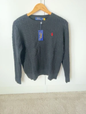 Svart kabelstickad tröja Polo Ralph Lauren - Svart kabelstickad tröja från Polo Ralph Lauren med rund halsringning och den klassiska röda logotypen broderad på bröstet. Den är helt ny och säljer för bra pris då jag inte vill ha den längre 