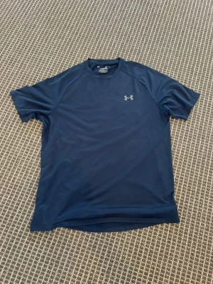 Mörkblå tränings-tshirt Under Armour - Snygg mörkblå tränings-tshirt från Under Armour med diskret logga på bröstet. Tillverkad i ett lätt och snabbtorkande funktionsmaterial som passar perfekt till träning. Klassisk rund hals och korta ärmar för en sportig look.