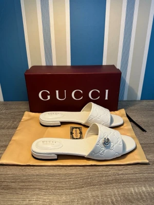 Gucci GG Embossed Sandals - Stilrena sandaler från Gucci i vit läder med GG-mönster och diskreta metalldetaljer. Sandaler är i mycket fint skick, sparsamt använda och väl omhändertagna. Originalbox och dustbag medföljer vid köp. Skriv om du har frågor! Kvitto finns