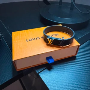 Svart armband - Elegant svart armband  med det ikoniska LV-mönstret. Armbandet har en stilren design och kommer i originalförpackning. Perfekt accessoar för att lyfta din stil.                   ! BOX INGÅR EJ ! 