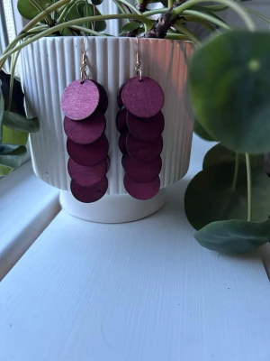Örhängen i trä - Säljer ett par coola statementörhängen i trä med flera stora, runda lila plattor som hänger i rad. Örhängena har krokar i metall och ger en unik och trendig look. Perfekta för dig som vill sticka ut med accessoarerna!