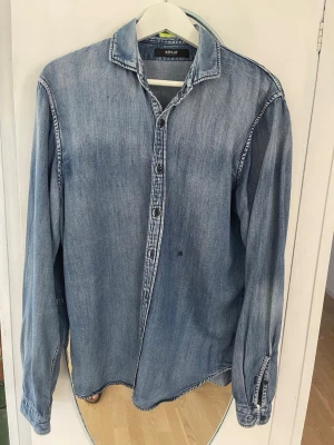Ljusblå jeansskjorta från Replay - Snygg ljusblå jeansskjorta från Replay med klassisk krage och knäppning framtill. Jackan har långa ärmar med knapp vid ärmslut och en avslappnad passform. Perfekt för dig som gillar en stilren och tidlös look.