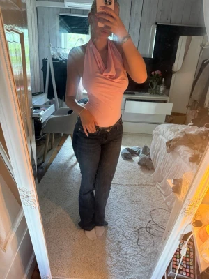 Mörkblå lågmidbade bootcut jeans - Säljer en ljusrosa halterneck topp med draperad front och djup urringning. Toppen är ärmlös och har en tight passform som framhäver figuren. Perfekt för dig som vill ha en enkel men snygg topp till sommaren.
