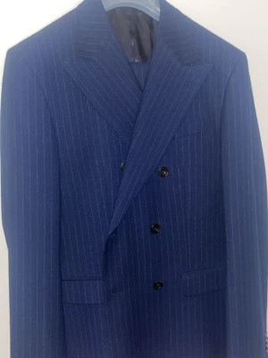 Blå randig kostym från Bläck - Snygg blå kostym från Bläck med smala vita ränder och klassisk dubbelknäppt kavaj. Skräddarsydd passform (tailored fit) och breda slag ger en stilren look. Storlek 50 byxor 52 kavaj