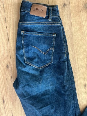 Mörkblå jeans från ONLY - Säljer ett par mörkblå jeans från ONLY med klassisk femficksdesign och snygga kontrastsömmar. Jeansen har rak passform och är tillverkade i ett mjukt denimtyg som är bekvämt. Perfekt för dig som gillar stilrena och tidlösa jeans.