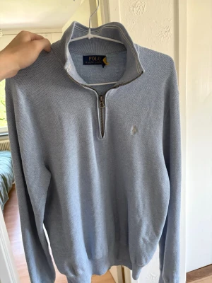 Ljusblå halvzip från Polo Ralph Lauren - Snygg ljusblå tröja från Polo Ralph Lauren med halv dragkedja och hög krage. Tröjan har diskret broderad logga på bröstet och är tillverkad i ett mjukt, stickat material. Perfekt för en clean och stilren look. Har kvitto vid intresse, köpte den för 2500 använd cirka 10-15 gånger 