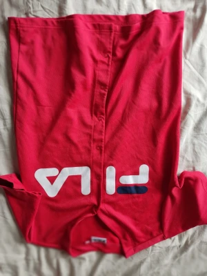 Röd FILA t-shirt med stor logga - Snygg röd t-shirt från FILA med stor vit och blå logga framtill. Tillverkad i ett lätt och luftigt material som passar perfekt till vardags eller träning. Klassisk passform och rund halsringning.