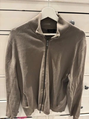 Beige ziptröja från Massimo Dutti - Snygg beige ziptröja från Massimo Dutti i extrafin bomull. Tröjan har hög krage, dragkedja framtill och två fickor. Perfekt för en stilren och avslappnad look.