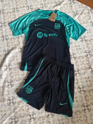 Barcelona träningsset Nike blå/turkos - Barcelona fotbollsset i storlek M. Shortsen har fickor med dragkedjor. Helt nya och oanvända, perfekt till sommaren. Hör gärna av vid frågor!