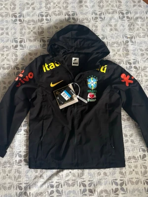 Nike Brasil svart vindjacka med huva - Svart brasil windbreaker i storlek M, helt ny och oanvänd, hör gärna av vid frågor!