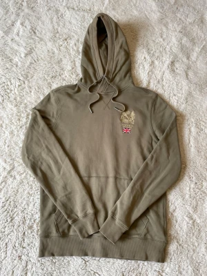 Olivgrön hoodie från Morris - Riktigt snygg hoodie från Morris. Tröjan har ett pyttelitet hål på övre delen av höger arm men inget som märks. Kontakta vid funderingar!