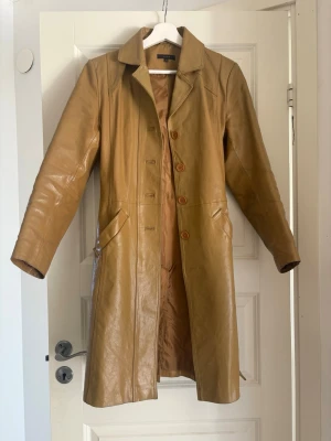 Äkta läderkappa - Vintage VILA läderkappa i äkta läder. Camelbrun färg, figursydd modell med midjebälte och fickor. Mycket fint skick. Storlek S.