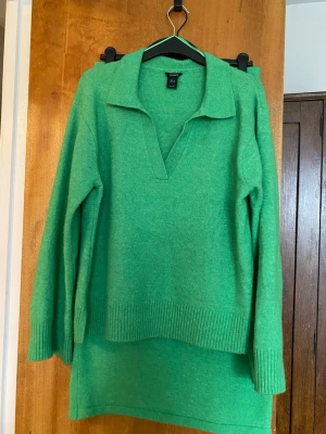 Grönt stickat set från Lindex - Säljer ett grönt stickat set från Lindex med en långärmad tröja med krage och v-ringning samt en matchande rak, midilång kjol med resår i midjan. Båda delarna är i mjukt stickat material och sån härlig grön färg!