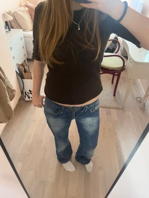 Blå baggy bootcut jeans med låg midja - Säljer ett par blå baggy jeans med låg midja och avslappnad passform. Jeansen har klassiska fem fickor, slitningar och ljusare partier framtill för en cool vintage-look. Perfekta för dig som gillar en avslappnad och trendig stil.