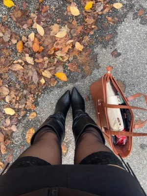 Svarta höga boots med klack - Säljer ett par svarta boots med hög klack och spetsig tå. Stövlarna har en slouchy design och är tillverkade i ett glansigt material som liknar skinn. Perfekta för att lyfta vilken outfit som helst och ger en edgy vibe.