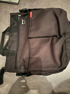 Skötväskafrån Skip Hop Duo inkl skötbädd - Säljer en svart skötväska från Skip Hop Duo med flera fack, dragkedja och justerbar axelrem. Väskan har praktiska handtag, metallspänne och är tillverkad i slitstark textil. Perfekt för dig som behöver en rymlig och funktionell väska till vardagen. Den är svart, ser. Run ut på bilden dock. Nytvättat, dock försvann några fläckar inte inne i väskan. Önskas kort så skickar jag via meddelanden.