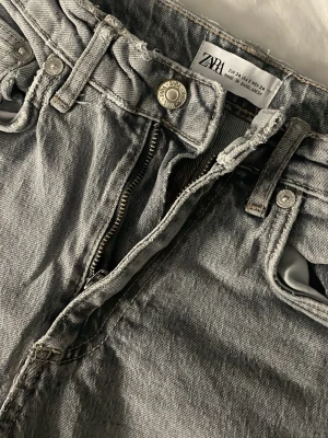 Grå raka jeans från Zara - Säljer ett par grå raka jeans från Zara med klassisk femficksmodell och dragkedja. Jeansen har bälteshällor, knappstängning och en snygg tvättad look. Perfekta till en avslappnad stil och passar till det mesta i garderoben.💖