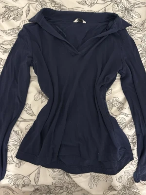 Mörkblå långärmad topp med krage - Snygg mörkblå långärmad topp med krage och v-ringning. Tröjan har en smal passform och är tillverkad i ett mjukt, stretchigt material som känns skönt mot huden. Perfekt för dig som gillar en enkel men stilren look.