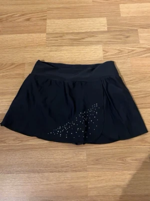 Konståknings kjol - konståkningsshorts i stretchigt träningsmaterial med insydda shorts under. Har glitter framtill och en slit som ger en fin detalj. Använda få gånger, i mycket bra skick – ser nästan nya ut.