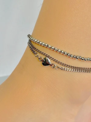 Fotlänk  - Fotlänk med silverfärgad hjärta och 2 kedjor i rostfritt stål med ett band av silverfärgade pärlor ihopsatt med skruv lås. 