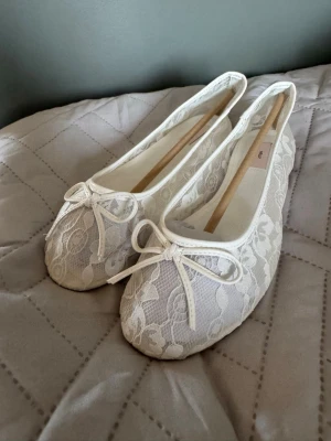 Vita spetsballerinaskor från nelly - Säljer ett par helt oanvända vita ballerinaskor från nelly med romantisk spets och rund tå. Skorna har en söt rosett framtill och är täckta av ett blommigt spetsmönster. Perfekta för dig som gillar en feminin och stilren look. Säljer dem då dem var förstora för mig.