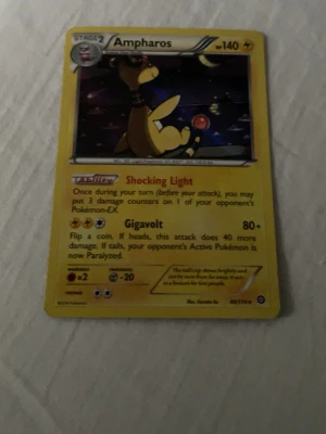 Pokémonkort Ampharos 140HP - Säljer ett Ampharos Pokémonkort med 140HP från XY Breakpoint-serien. Kortet har gul ram, motiv av Ampharos och attacker som Shocking Light och Gigavolt. Baksidan har klassiskt blått Pokémon-mönster med Pokéboll. Perfekt till samlingen!