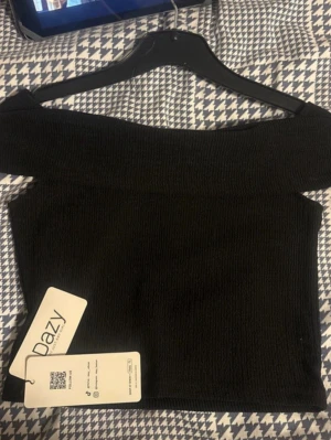 Svart offshoulder t -  svart offshoulder topp. Toppen är tight och har en bred kant över axlarna som ger en snygg siluett. 
