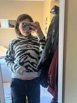 Zebramönstrad stickad tröja - Cool stickad tröja med zebramönster i svart och vitt. Tröjan har en hög krage och ribbstickade muddar vid ärmslut och nederkant. 