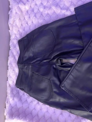 Svarta fuskskinnbyxor raka ben - Snygga svarta byxor i fuskskinn med raka ben och klassisk femficksmodell. Byxorna har hög midja och stilrena sömmar, perfekta för en trendig look. Passar till allt från oversized tröjor till crop tops.