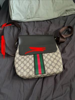 Väska - En väska med gg tryck och en grön röd rand över mitten. Brunt läder överkast och brunt axelband. Perfekt för dig som vill stuka ut. 