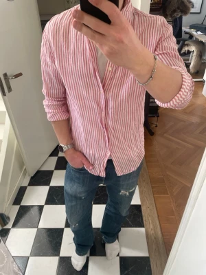 Rosa randig linneskjorta  - Tja säljer en snygg linneskjorta från märket Martinique. Skjortan är i utmärkt skick och har bara använts 1-2 gånger. Tröjan är i storlek M men passar även L. Modellen på bilden är 175 72 kg. Skriv vid fler frågor och funderingar 