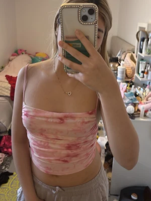 Rosa tie-dye tubtop med smala axelband - Säljer en rosa och vit tie-dye tubtop med smala axelband. Toppen är figurnära och har en mjuk, stretchig känsla som passar perfekt till sommarens outfits. Materialet ser ut att vara bomull eller polyesterblandning.