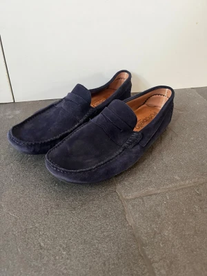 Mörkblå mocka loafers Portobello - Snygga mörkblå loafers från Portobello i mjuk mocka med klassisk pennyloafers-design. Skorna har en stilren siluett och bruna innersulor med Portobello-logga. Perfekta för en avslappnad men ändå uppklädd look.