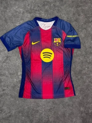 FC Barcelona matchtröja Nike - Snygg FC Barcelona matchtröja från Nike med klassiska blå och röda vertikala ränder. Tröjan har klubbmärke, Nike-logga och Spotify-logga på bröstet samt tryck på ärmen. Tillverkad i lätt och ventilerande material, perfekt för fotboll eller träning.