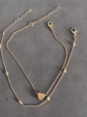 Fotlänk  - Fotlänk med 2 delar: 1 st dekorerad med ett hjärta, 1 st dekorerad med kulor. Materialet äralloy. (#269)