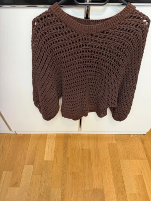 Brun virkad stickad tröja - Säljer en brun stickad tröja med virkat mönster och rund halsringning. Tröjan har en luftig och oversized passform med långa ärmar. Perfekt för lager-på-lager och att styla med jeans eller kjol.