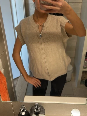 Beige stickad väst från Luella - Beige stickad väst från Luella med dragkedja framtill. Västen har korta ärmar och en avslappnad passform, perfekt att bära över en t-shirt eller skjorta eller bara som den är. Sååå skön i alpaca material. Köpte denna i England för 1000kr🩷