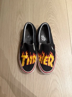 Vans Thrasher str 38 - Vans Thrasher sneakers joggesko i størrelse 38. Skoene er svarte med flamme- og Thrasher-logo på toppen. Slip-on design uten snøring, laget i tekstil og gummi. Kan vaskes gratis av meg med professionell skovasking utstyr!  Kan leveres eller hentes i Frogner <3