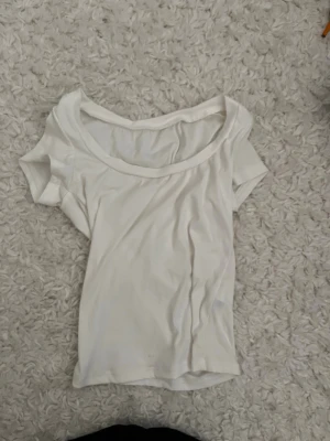 Vit basic t-shirt med bred urringning - En enkel vit t-shirt med bred urringning och korta ärmar. Perfekt till jeans eller kjol för en clean och avslappnad look. Tillverkad i mjuk bomull som känns skön mot huden.