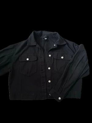 Svart jeansjacka från H&M - Svart jeansjacka från H&M med klassisk krage, två bröstfickor med lock och silverfärgade knappar. Jackan har en rak passform och långa ärmar. Inga defekter! 🖤
