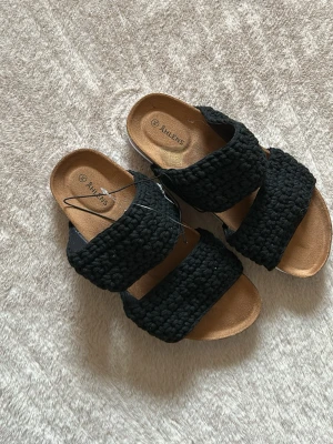 Svarta sandaler från Åhléns - Helt oanvända sandaler från Åhléns med två breda, stickade remmar och mjuk innersula i beige. Sulan är vit undertill och sandalerna har en avslappnad slip-in design. Perfekta för sommaren💕