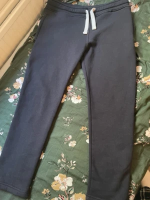 Mörkblå mjukisbyxor med dragsko - Säljer ett par mörkblå mjukisbyxor med vita dragsnören i midjan och en bakficka. Byxorna har en klassisk rak passform och är gjorda i mjukt, bekvämt material som passar perfekt för chill dagar. Inga synliga loggor eller märken.
