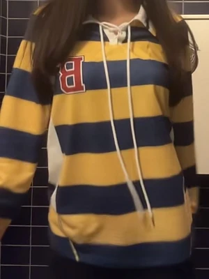 Randig hoodie med B-märke - Gul och marinblå tröja med breda ränder och vit snörning i halsen. Stor röd bokstav B på bröstet och vita detaljer vid sidorna. Hoodien har huva och sportig collegekänsla, perfekt för en avslappnad stil.