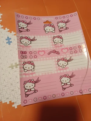 Hello Kitty etiketter rosa ark - Säljer ett ark med söta Hello Kitty etiketter i rosa och vitt. Motiven visar Hello Kitty med rosett och blommor, perfekt för att märka böcker, presenter eller prylar. Materialet är glansigt papper och arket har flera olika etikettstorlekar.