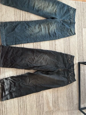 Två par baggy jeans i blått och svart - Säljer två par baggy jeans, ett par i klassiskt blå denim och ett par i svart. Båda har fem fickor och normal midja. Perfekta för en avslappnad och trendig look. Passar dig som gillar enkel och stilren design. Svarta jeansen är från Weekday, blå(?)