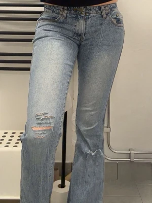 Ljusblå slitna bootcut jeans - Säljer ett par ljusblå bootcut jeans med slitningar på vänster lår och knä. Jeansen har klassisk femficksmodell, hög midja och är tillverkade i denim. Perfekta för en avslappnad och trendig look. Liten mini reva vid rumpan (se bild 4) men går lätt att laga med lite nål o tråd💞 Jag brukar ha storlek 25/34 och är 176  cm lång o dessa är lite korta för mig