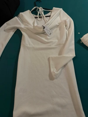 Vit långärmad kortklänning Lager 157 - Stilren vit kortklänning från Lager 157 med lång ärm och lätt struktur i tyget. Klänningen har en snygg omlott-detalj vid halsen och knytband i nacken för extra detalj. Perfekt för dig som gillar minimalistisk och modern stil.